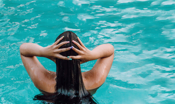 Back view female tourist in swimwear touching wet hair in pool with pure water during vacation
