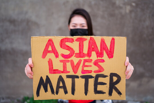 Ethnic female in mask and with carton placard with inscription Asian Lives Matter protesting in city street and looking at camera