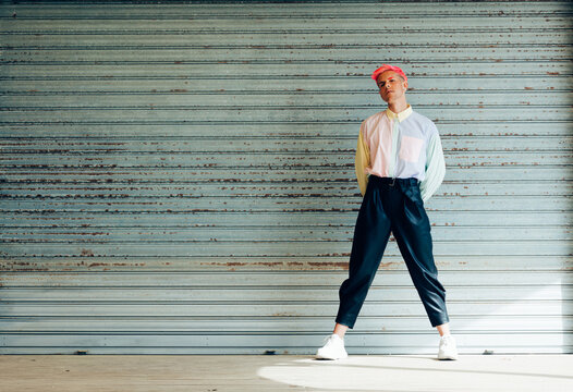 Self confident young gay in trendy apparel with pink hair and tattoos looking at camera