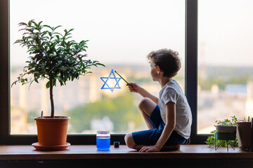 Little Jewish boy draws the Star of David sign on the window. The symbol of Israel. Solidarity...