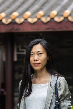 Portrait of beautiful Asian woman walking near traditional architecture building in garden looking at camera