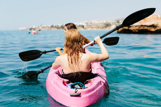 Back view travelers with paddles floating on turquoise seawater near the rocky shore on sunny day in Malaga Spain