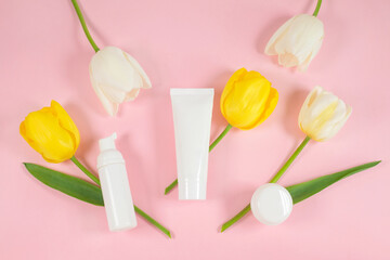 White cosmetic bottles containers on yelolow and white tulips flowers.