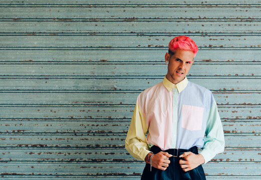 Self confident young gay in trendy apparel with pink hair and tattoos looking at camera
