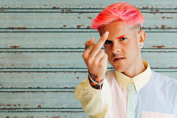 Homosexual man in striped shirt with tattoo and pink hair demonstrating middle finger while looking at camera