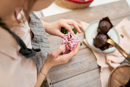 High angle of crop anonymous female with blossoming flower sprig above table with baked dessert during cooking process at home