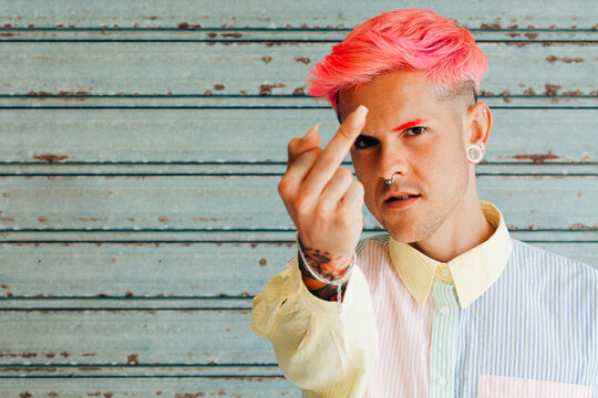 Homosexual Man In Striped Shirt With Tattoo And Pink Hair Demonstrating Middle Finger While Looking At Camera