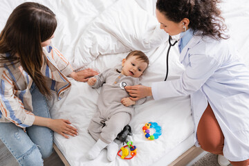 top view of african american pediatrician in white coat examining baby boy with stethoscope