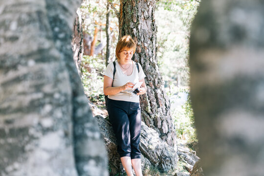 Mature female hiker text messaging on cellphone among trees in woods of Aran Valley in Lleida Catalonia Spain