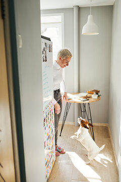 Content female astrologist playing with small purebred dog while looking at each other in house