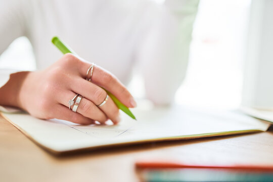 Crop of anonymous female astrologist taking notes in notepad at desk at home in sunlight