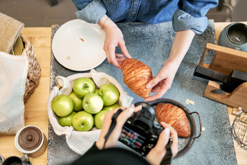 From above of crop anonymous female taking photo of delicious pastry on camera against girlfriend at kitchen table