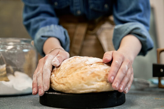 Crop anonymous woman with whole fresh wheat bread with crust at table during cooking process