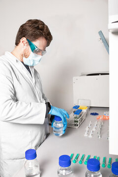 Side view of male biologist in protective glasses and mask opening bottle with liquid at table in cannabis laboratory