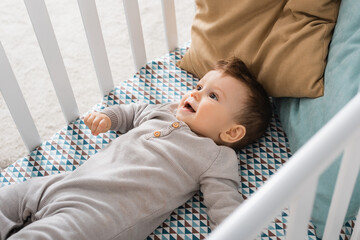 high angle view of infant boy lying in baby crib - obrazy, fototapety, plakaty
