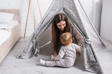 happy mother looking at baby son sitting near tipi in bedroom © LIGHTFIELD STUDIOS