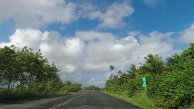 POV Driving along two lane road on tropical island against blue sky and clouds