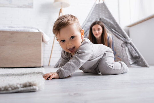 excited baby boy crawling on floor near mother on blurred background