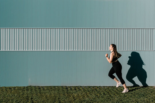 Side view of curvy young athletic woman running outdoors in the afternoon - Healthy lifestyle and slim down concept - Copy space for text
