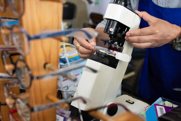 A skilled technician uses a microscope to look at the eyeglasses lenses. To measure the size for the customer at the eyeglass shop