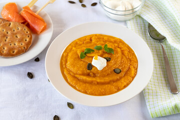 Cream of pumpkin soup with whipped cream and crackers isolated on white blanket with salmon rolls on a wooden skewer.