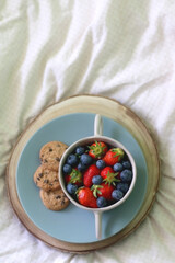Bowl of blueberries and strawberries and chocolate chip cookies on a bed. Flat lay.