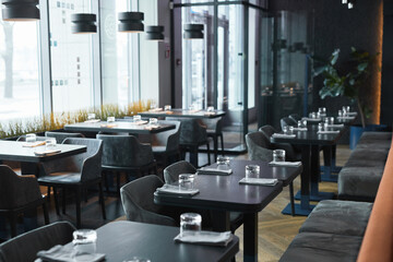 Modern interior of restaurant in gray color furnished soft chairs and black tables with glasses and...