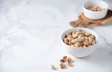 Pistachio nuts in a white bowl on a white  marble background. Front view and copy space
