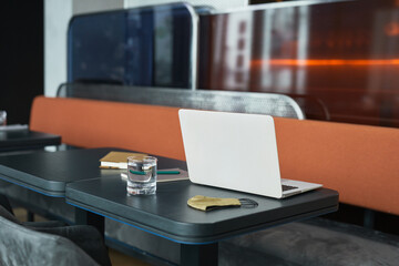 Workplace in modern cafe: open laptop, cloth mask, glass of water and notepads in black table