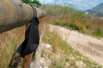 black covid mask hanging from a pole, abandoned on the side of the road in the middle of nature