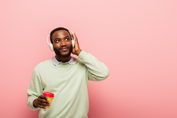 Obraz premium African american man in headphones holding paper cup on pink background