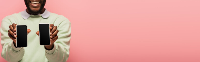 Cropped view of african american man holding smartphones isolated on pink, banner