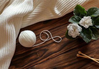White draped fabric, white ball of yarn, knittind needles and white violet on wooden background. Home hobbies concept.