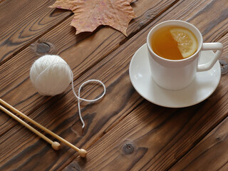 Cup of green tea, ball of white yarn, knitting needle and yellow maple leaf on wooden table