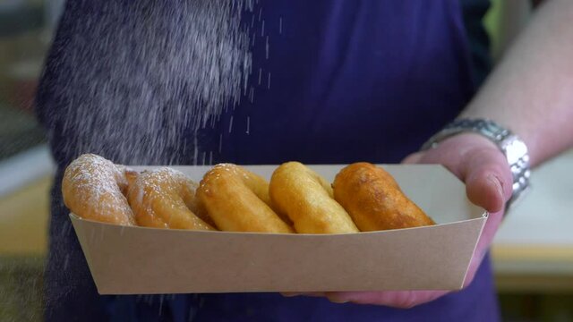 Chef sprinkles set of donuts with powdered sugar close-up. Spreading sugar powder on donuts. Slow motion