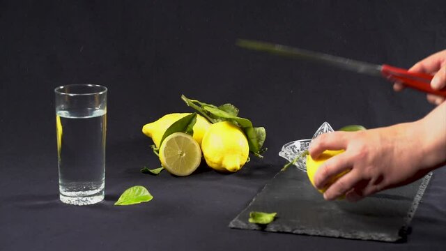 Woman squeezing a juice from fresh lemons, on black background