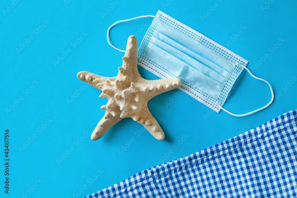 Wall mural medical face mask near beach towel and starfish on a blue background, top view, beach items and summ