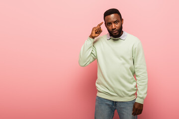 Fototapeta premium African american man looking at camera while pointing at head on pink background