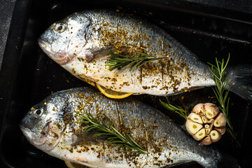 Raw fish dorado in baking sheet at black stone table. Ready for cooking. Top view with copy space.