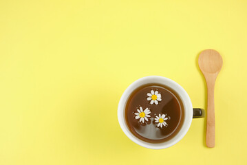 Cup with an infusion or chamomile tea on yellow background and a wooden spoon with space for text and full depth of field