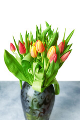 Tulips with leaves in a vase on white, selective focus.