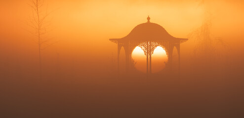 Gazebo on a background of the sun in the fog at dawn