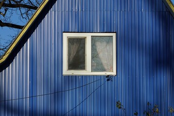one white window on the blue metal wall of the attic of a private house on the street