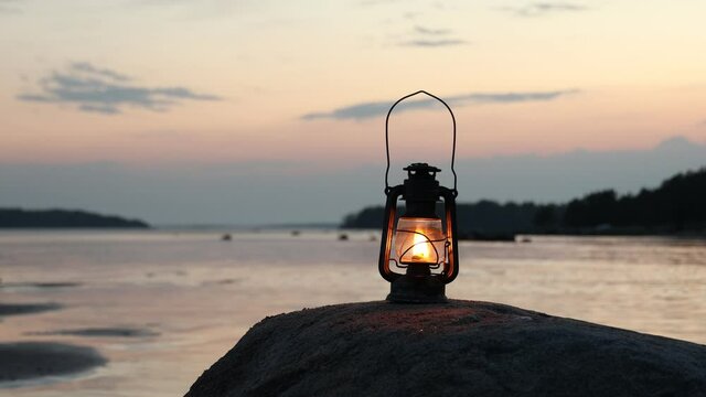 Vintage oil lamp on the sea at sunset. Lantern burning with an orange soft flame. Blurred background.