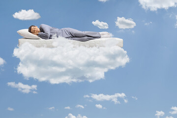 Man in pajamas sleeping on a mattress and floating on clouds