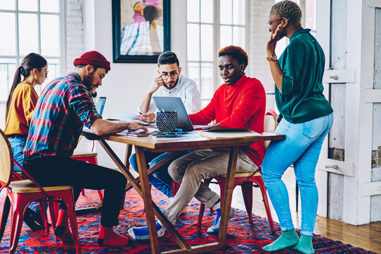 Group of diverse students collaborating on university course work while preparing to university exams in coworking space, male and female bloggers discussing content text for laptop promotion