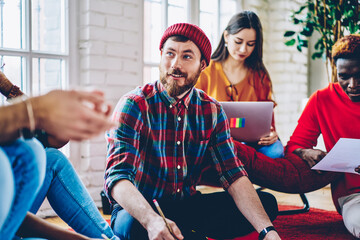 Obraz premium Bearded Caucaisan male freelancer dressed in casual shirt and hat communicate with remote colleagues during brainstorming meeting for collaborate together, group of young students e learning indoors