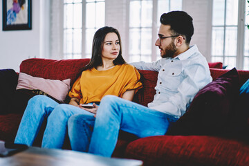 Multicultural couple in love talking and discussing plans during weeknd time in apartment, Turkish boyfriend communicating with Caucasian girlfriend resting at cozy sofa in stylish living room