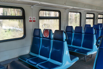 Fototapeta premium Empty wagon in train with blue chairs and red round stickers with restriction that forbid to take up middle seat in row to reduce number of passengers.. Traveling in new reality, covid restrictions