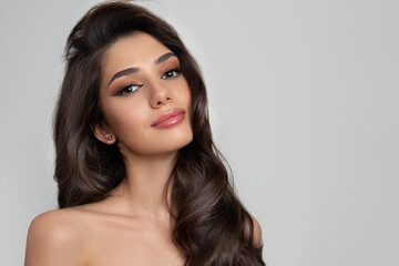 Portrait of a brunette with curly shiny hair and makeup. Gray background